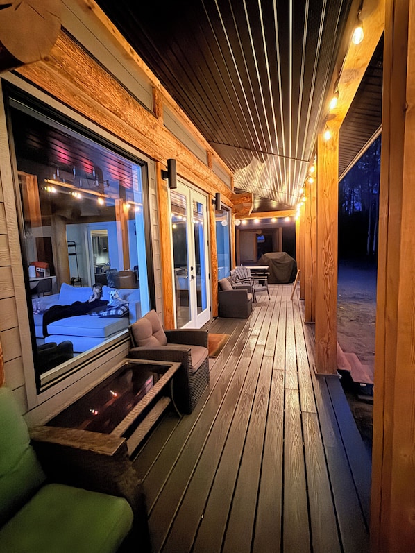 A covered outdoor seating area with wooden flooring, cushioned seating, and a glass enclosure for a view.
