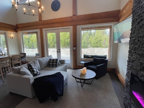 A cozy living room with a sofa, chairs, a coffee table, and a fireplace. - McCulloch Lake Chalet – Private Hot Tub, Lake Views, Dog-Friendly, Sleeps 12 (Naramata)