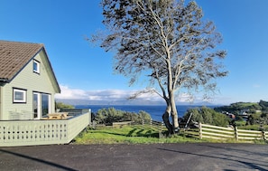 Une maison avec un grand arbre devant, une vue sur la mer et un ciel dégagé.