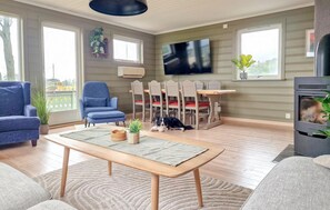 A living room with a sofa, armchair, dining table, chairs, a TV, and a fireplace.