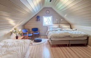 Ein gemütliches Schlafzimmer im Dachgeschoss mit schrägen Wänden, einem Bett, zwei Stühlen, einem kleinen Tisch mit einer Pflanze und einem Fenster, das natürliches Licht hereinlässt.