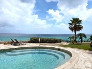 Ein Pool mit gewölbter Kante, Liegestühle und Blick aufs Meer.