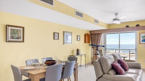 Un'area pranzo con un tavolo apparecchiato per quattro persone, un divano e un balcone vista mare.