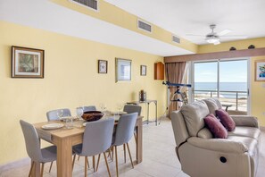 Ein Essbereich mit Tisch für vier Personen, einer Couch und einem Balkon mit Meerblick.