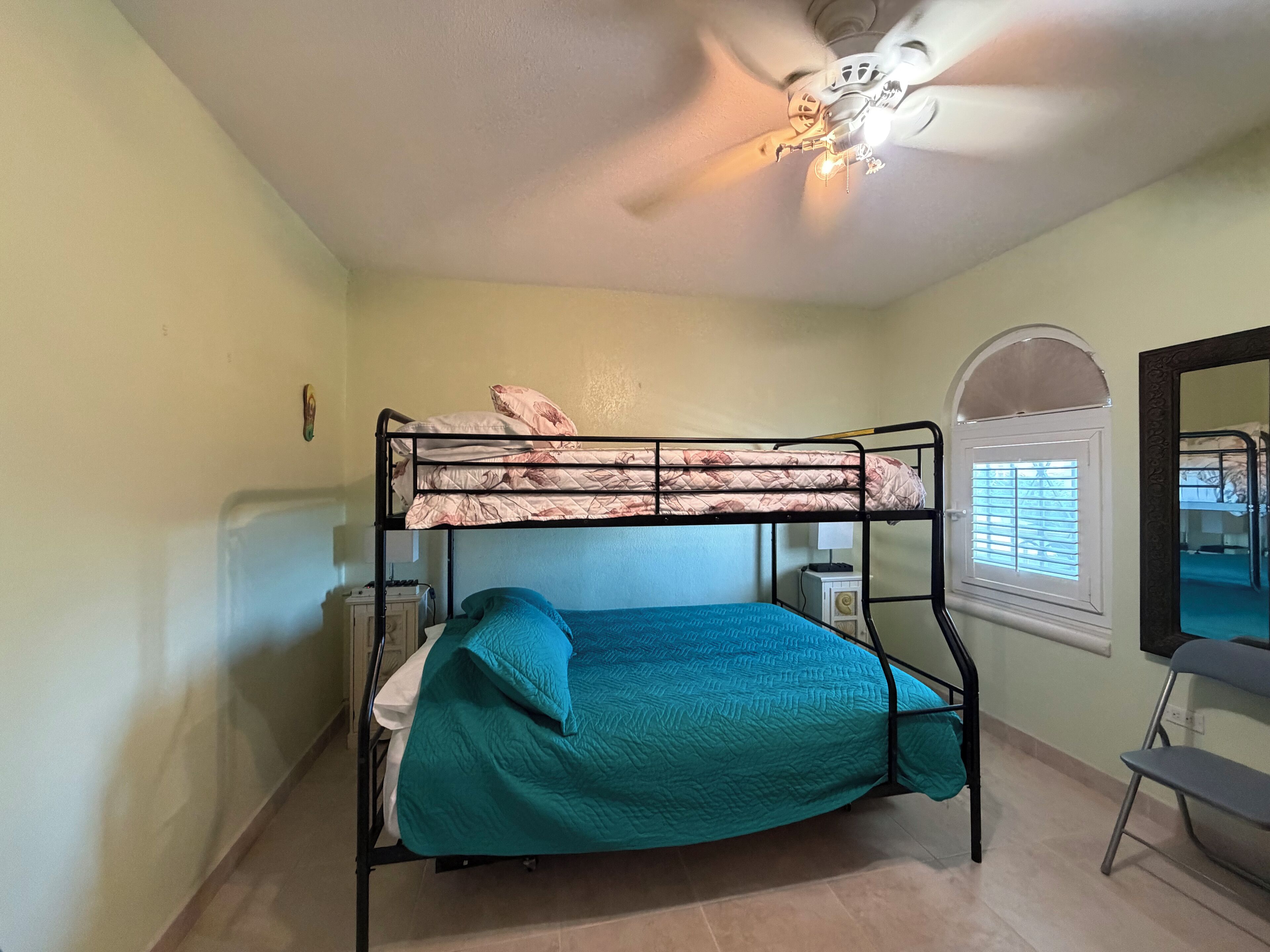 A bunk bed with a ceiling fan, a window with blinds, and a mirror on the wall.