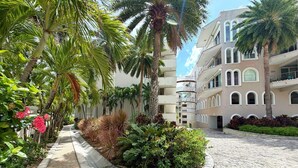Un cortile con vialetto lastricato, palme e un edificio con diversi balconi.