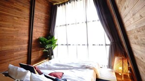 Un dormitorio con cama, planta en maceta y ventana con cortinas.