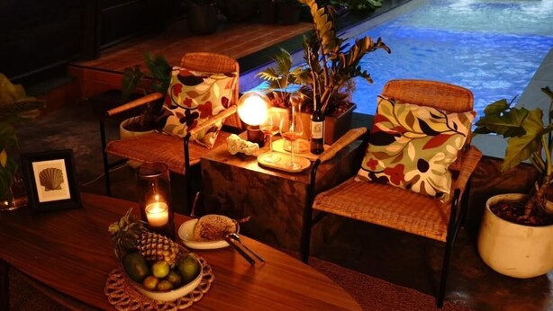 Comedor con vista a la piscina, que incluye una mesa de madera, sillas de mimbre y plantas en macetas.
