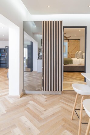 Een modern interieur met een visgraat parketvloer, een eethoek met witte stoelen en een in de achtergrond zichtbare keuken.