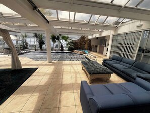 Ein großzügiger Innenbereich mit einer großen Sitzecke, einem Pool und Blick ins Freie.