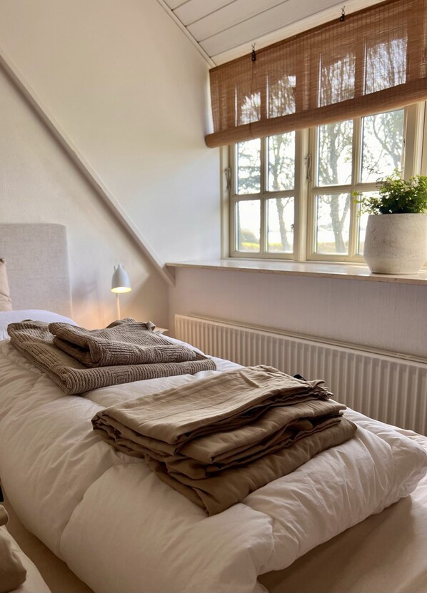 A bedroom with a bed, a window with a view of trees, a radiator, and a bedside lamp.