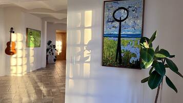 A hallway with a guitar, a plant, and a painting of a landscape with a circular motif.