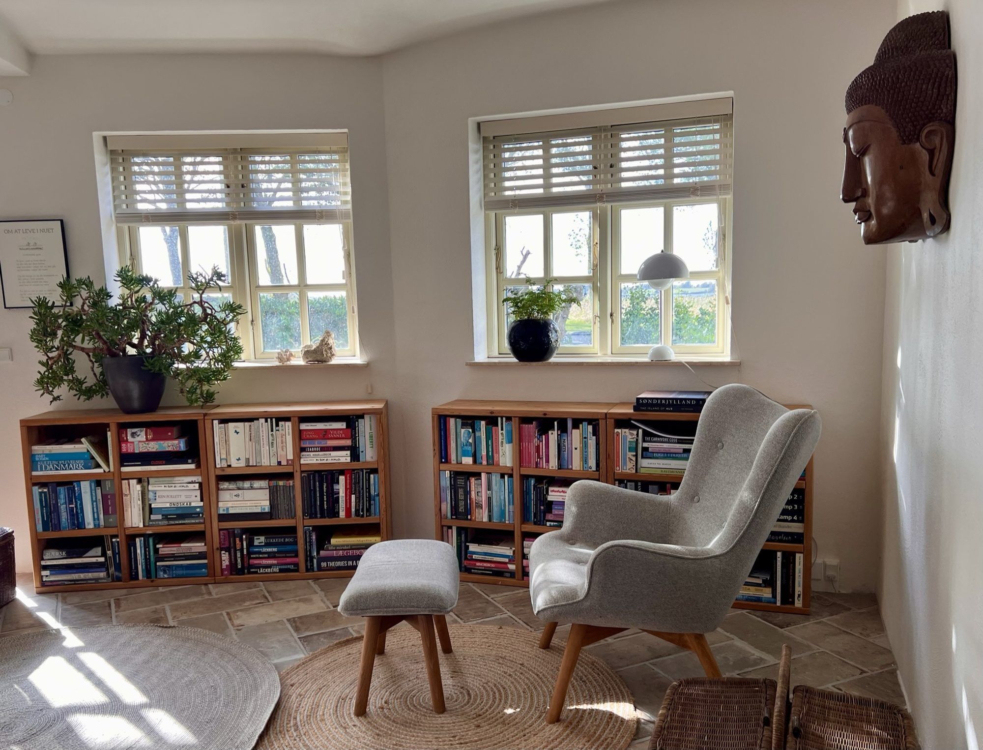 A room with two windows, a bookshelf, a chair, and a statue.