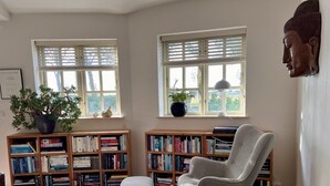 A room with two windows, a bookshelf, a chair, and a statue.