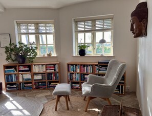 A room with two windows, a bookshelf, a chair, and a statue.