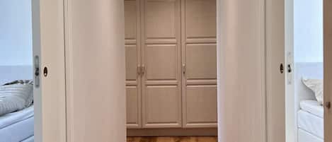 A hallway with wooden flooring leading to a bedroom with a bed and a window.