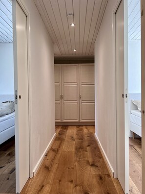 A hallway with wooden flooring leading to a bedroom with a bed and a window.