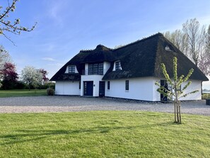 A two-story house with a thatched roof, white walls, and a gravel driveway.