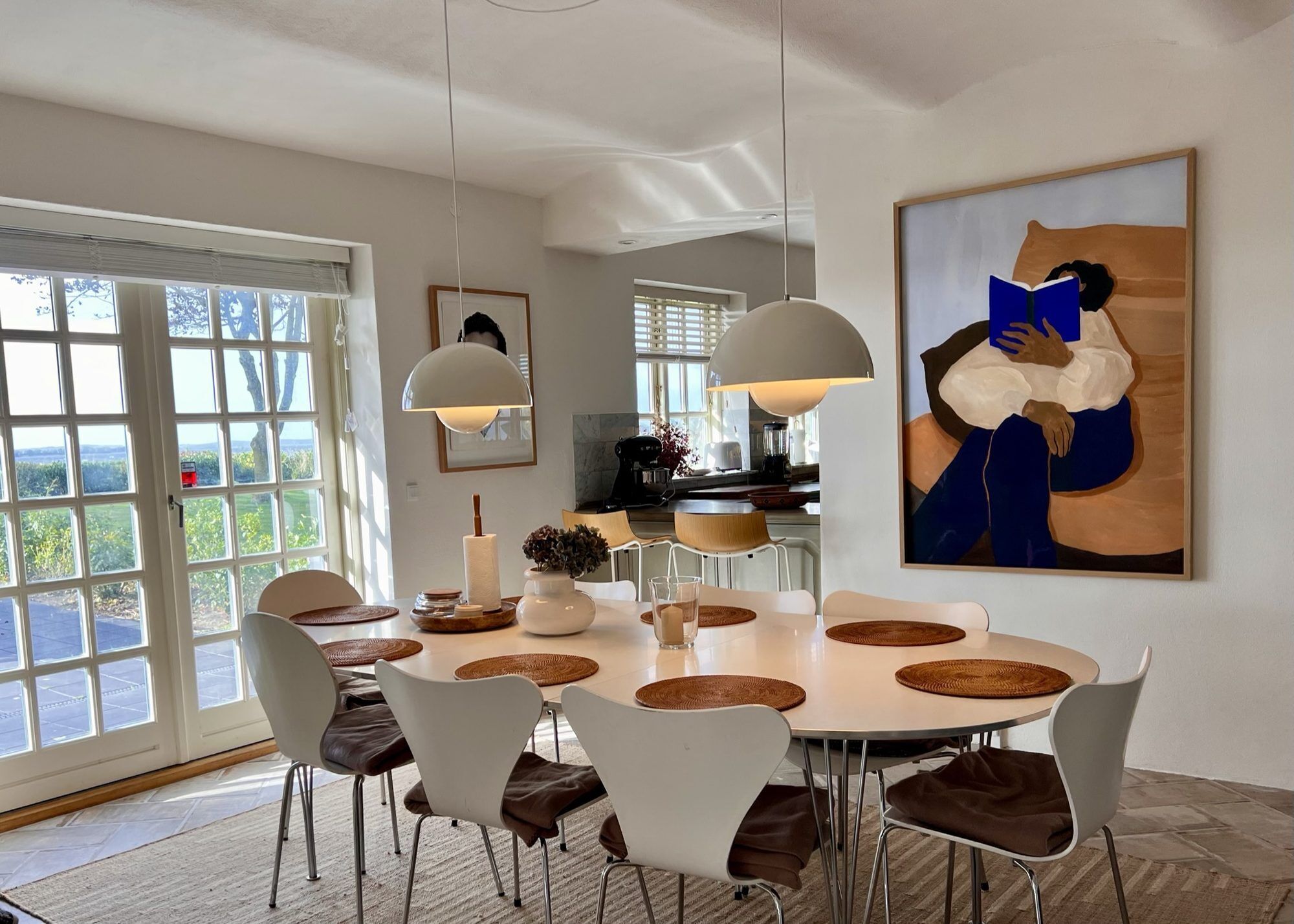 A dining area with a round table, white chairs, and a large painting on the wall.
