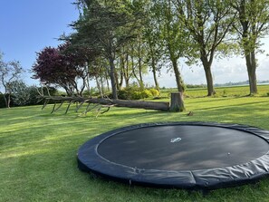 A trampoline on a grassy lawn with trees in the background.