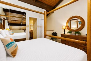 Ein Hotelzimmer mit einem grossen Bett, einem Holzkopfstück, einem runden Spiegel, einer Kommode und einem kleinen Tisch mit einer Lampe.