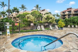A swimming pool with a tiled edge, surrounded by lounge chairs and palm trees, with a building in the background. - Walk to Beach! Pool, Gym, Pickleball & More (Kihei)