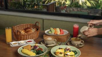 A breakfast setting with a wicker basket, croissants, fruit, coffee, and a person pouring tea.