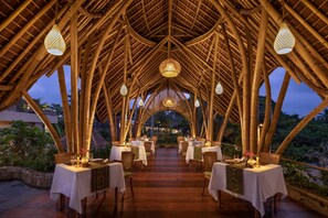 An outdoor dining area with bamboo structures, tables set for dining, and hanging lights. - Premadewi Resort A Pramana Experience (Ubud)
