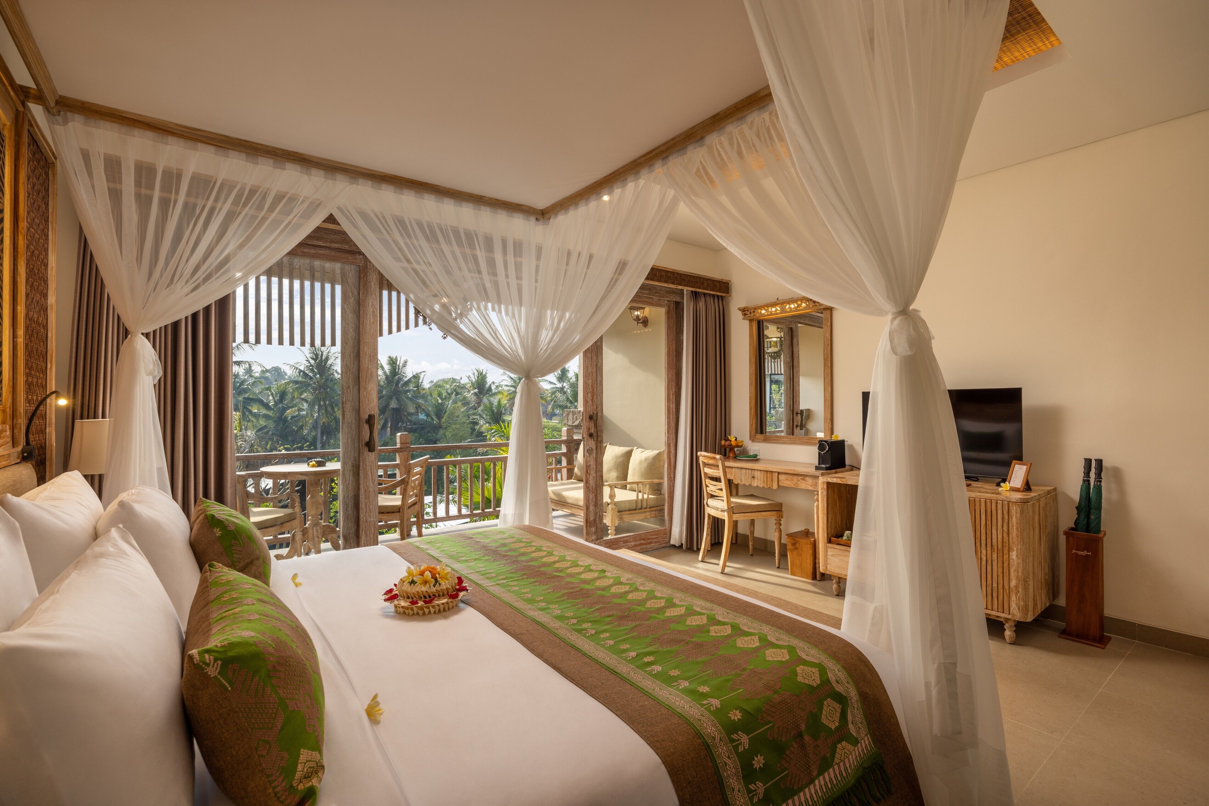 A hotel room with a bed, a desk, a television, and a balcony with a view of palm trees.