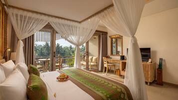 A hotel room with a bed, a desk, a television, and a balcony with a view of palm trees.
