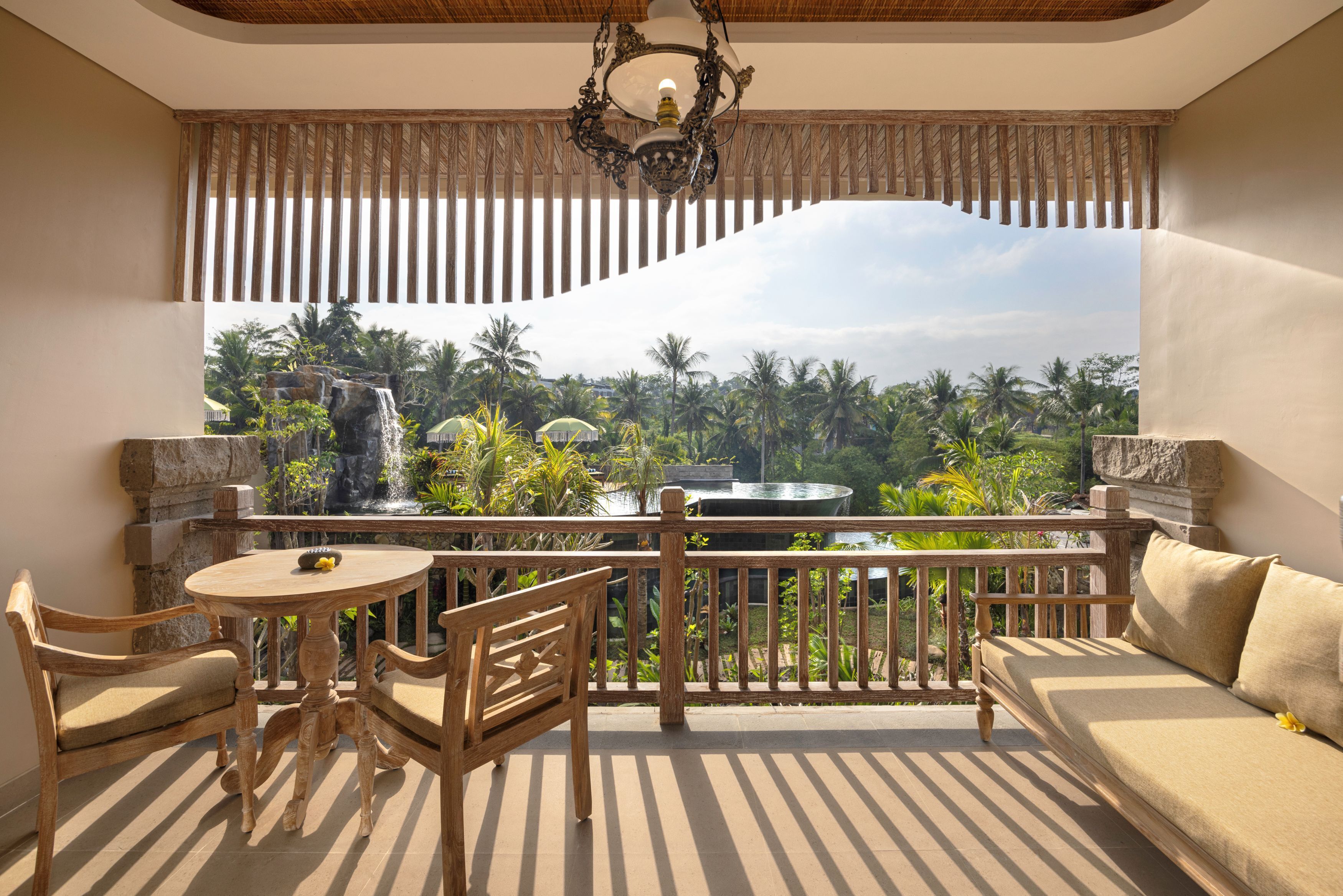 Un balcon offrant une vue sur une cascade et des palmiers, aménagé avec un canapé, des fauteuils et une table.