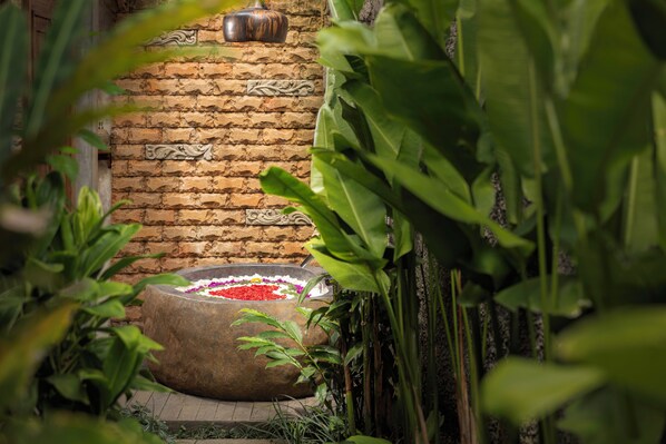 A stone basin with colorful flowers, a brick wall with decorative carvings, and lush green foliage.