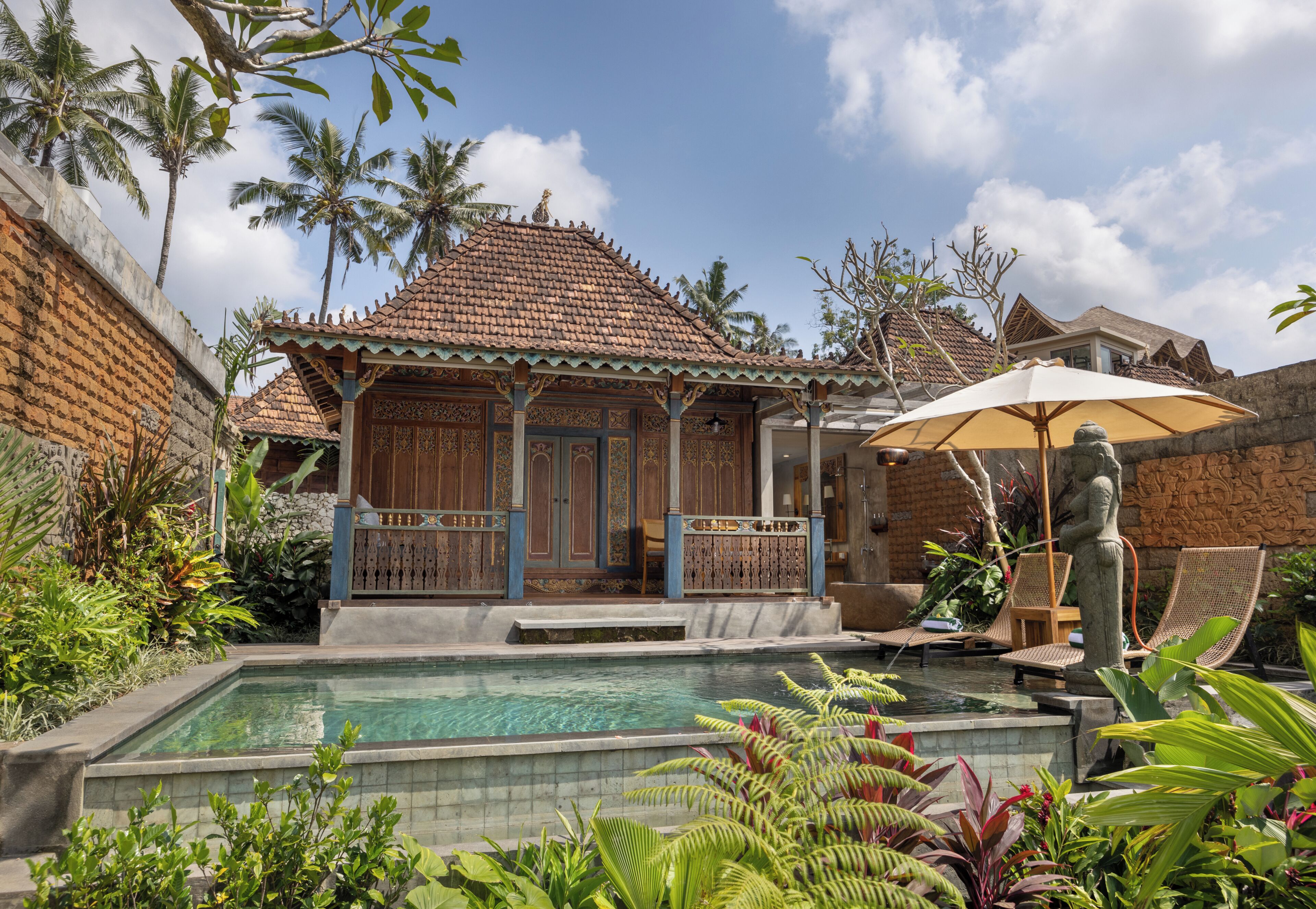 Un bâtiment traditionnel avec un toit en tuiles, une piscine et une végétation tropicale luxuriante.