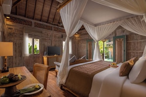 A room with a bed, a television, a dining table with a plate of food, and a window with a view of greenery.