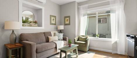 A living room with a sofa, armchair, small table, and a window with curtains.