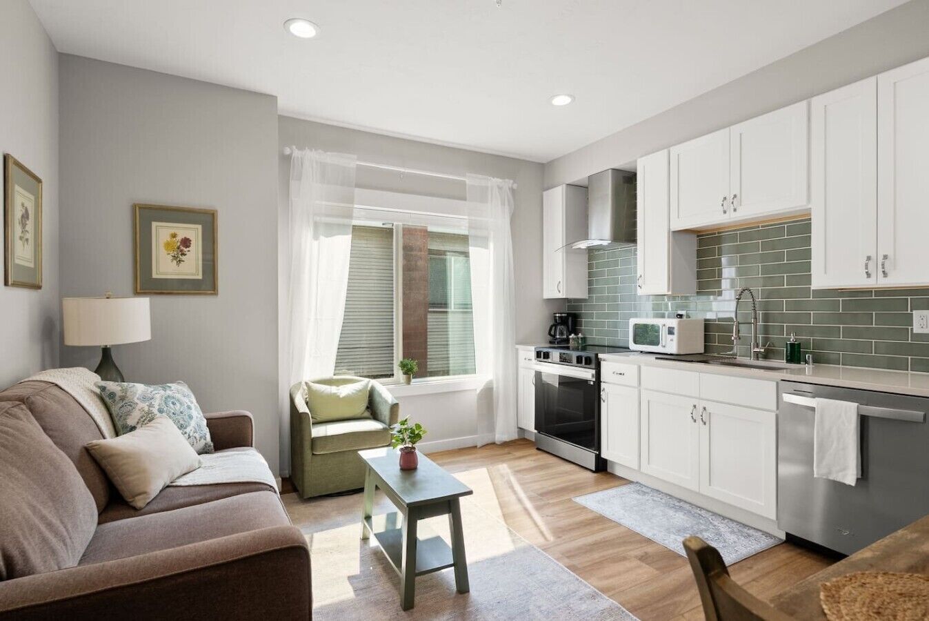 Un espace de vie compact comprenant un canapé, une petite table, une fenêtre avec des rideaux, une kitchenette équipée d’un four à micro-ondes et une cuisinière.