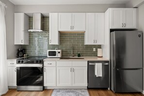 Une cuisine moderne avec des meubles blancs, un réfrigérateur en acier inoxydable, un four à micro-ondes, une cuisinière et un évier.