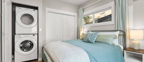 A bedroom with a bed, a washing machine, and a window with curtains.