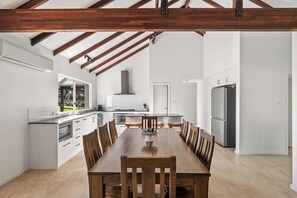 A modern kitchen with white cabinetry, a dining table with wooden chairs, and a large window. - Fermoy Lodge—Wine Country Haven & Vineyard Views (Wilyabrup)