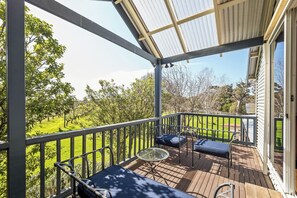 A covered outdoor deck with a table and chairs, overlooking a grassy area with trees. - Fermoy Lodge—Wine Country Haven & Vineyard Views (Wilyabrup)