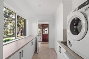 Ein Waschraum mit Waschmaschine, Spüle und Fenster mit Blick auf einen Garten.