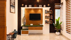 A modern living room with a flat-screen TV mounted on a wooden wall, a decorative vase, and a potted plant. - Maiibreeze Retreat (Sultan Bathery)