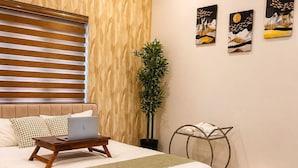 A bedroom with a bed, a laptop on a bedside table, a plant, and artwork on the wall. - Maiibreeze Retreat (Sultan Bathery)