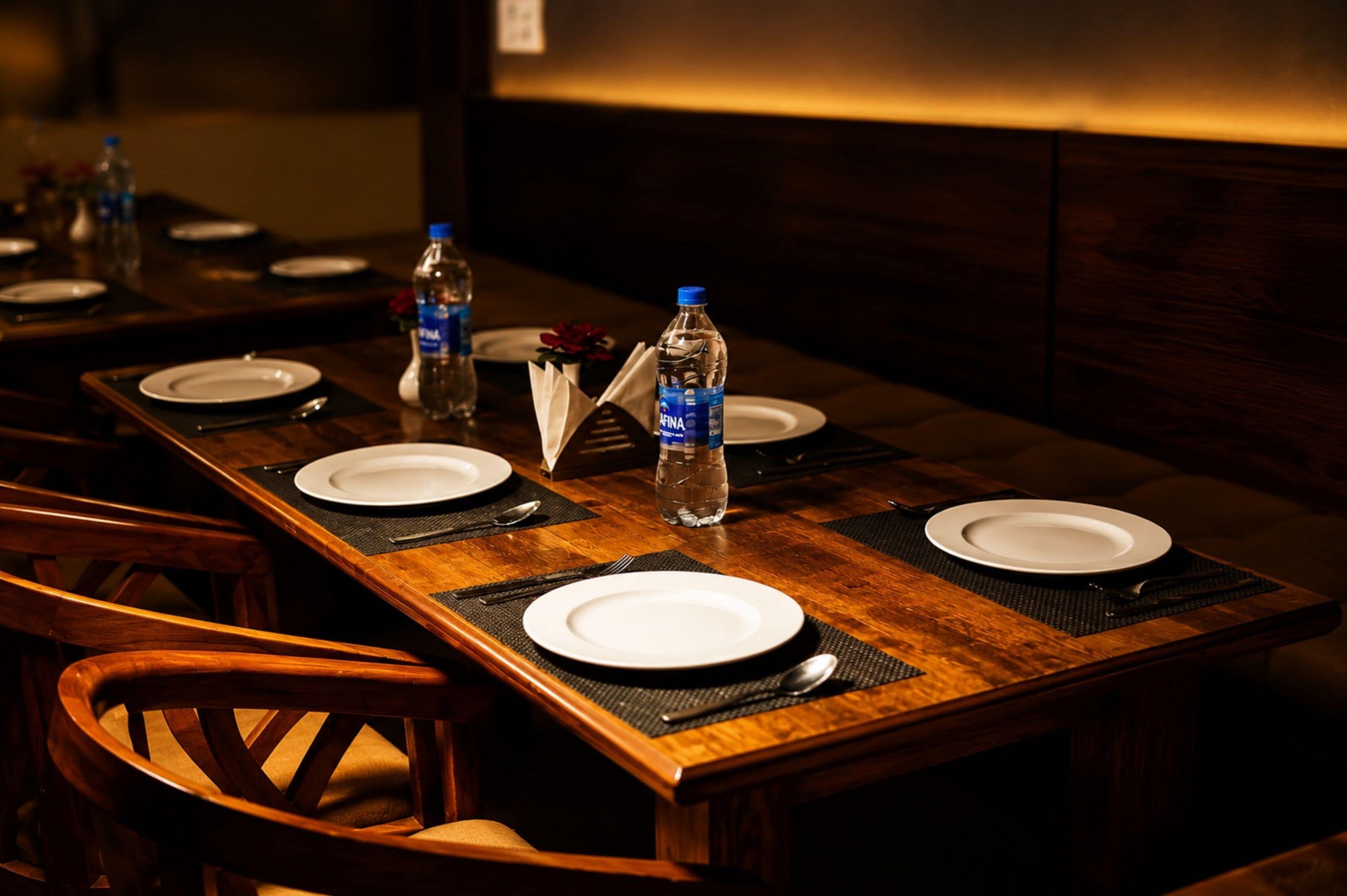 A dining table set with plates, cutlery, and water bottles, with chairs around it.