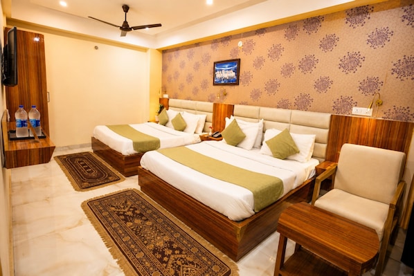 Habitación de hotel con dos camas, televisor, ventilador de techo y armario de madera.