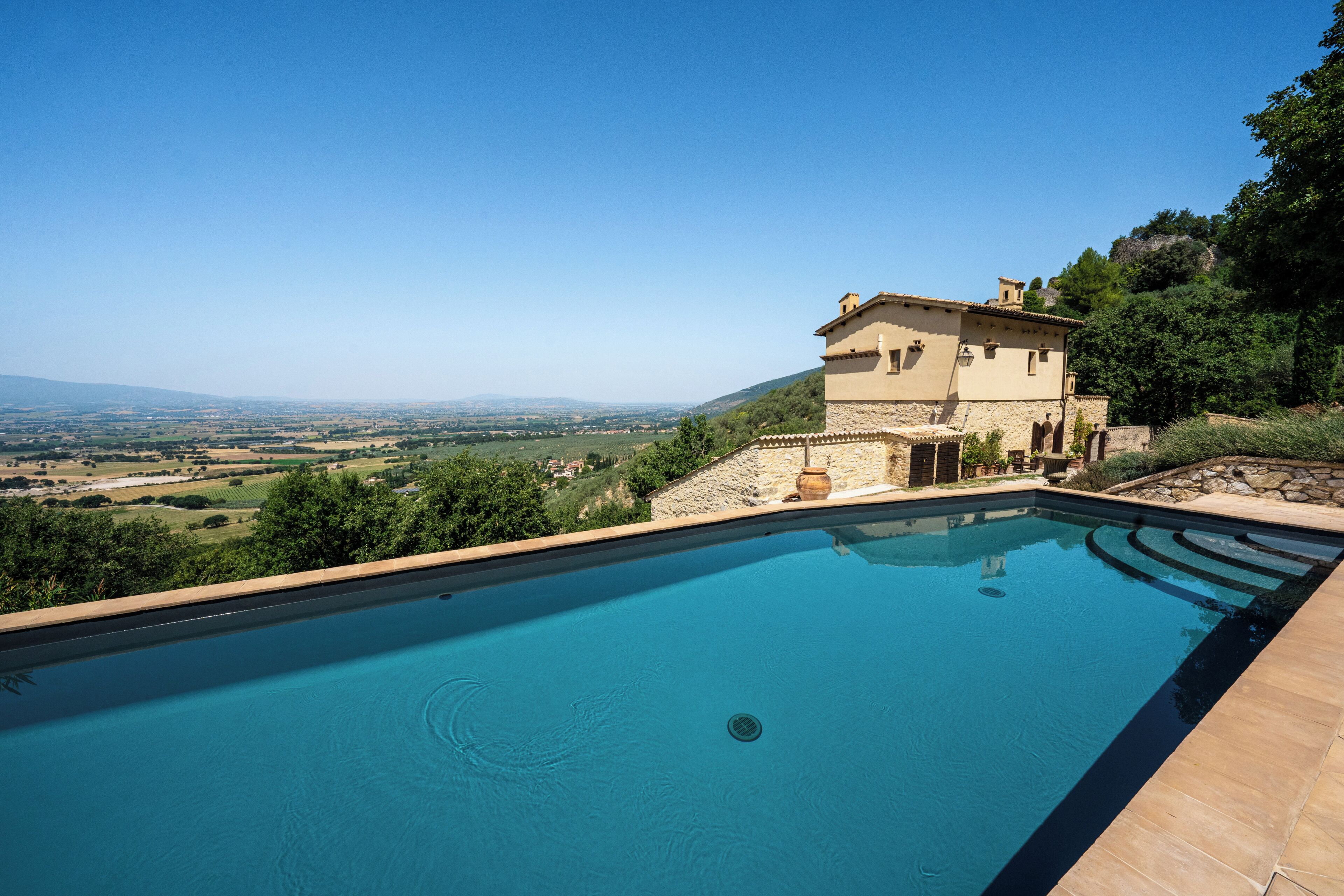 Piscina com vista para uma paisagem rural e um edifício com fachada de pedra.