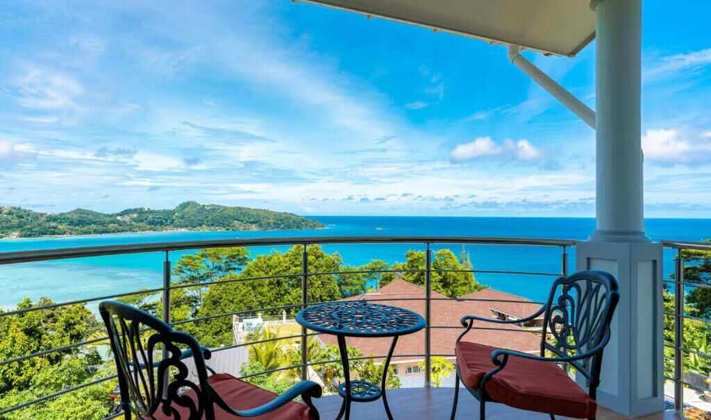 Un balcon avec une table et des chaises, offrant une vue imprenable sur un paysage côtier, avec une vue dégagée sur la mer et le lointain.