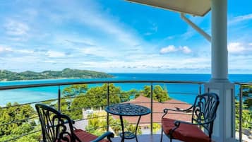 Ein Balkon mit Tisch und Stühlen, der auf eine Küstenlandschaft mit freiem Blick auf das Meer und das entfernte Land blickt.