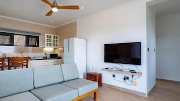 A modern living room with a grey sofa, a flat-screen TV mounted on the wall, and a ceiling fan.