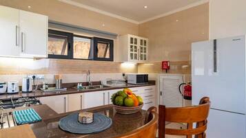 A modern kitchen with white cabinets, a gas stove, a microwave, and a fruit bowl on the counter.